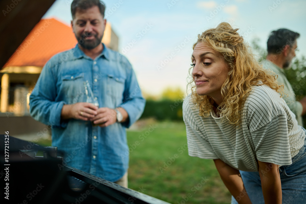 Naklejka premium Woman preparing barbecue with husband drinking beer in background