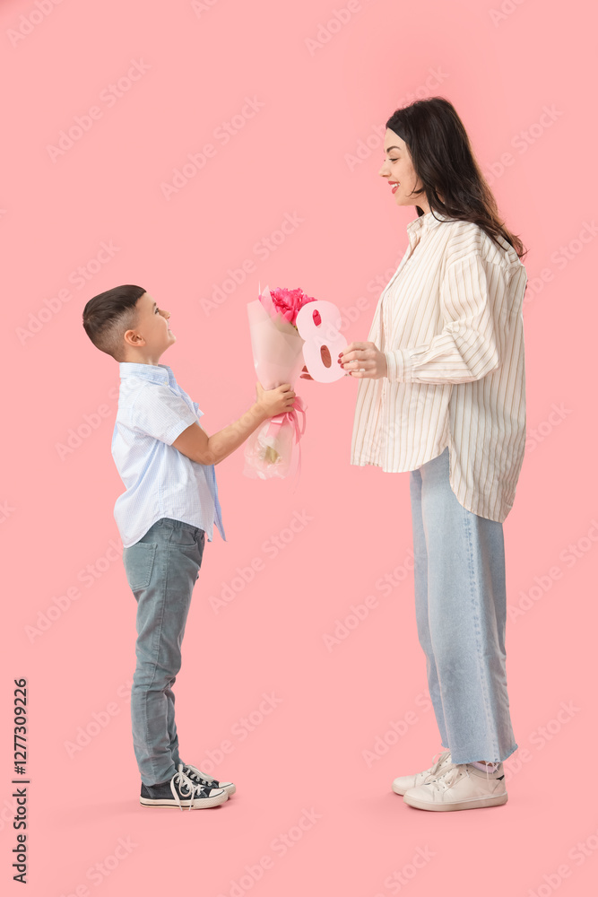 Cute little boy greeting his mother with International Women's Day on pink background Cute little boy greeting his mother with International Women's Day on pink background