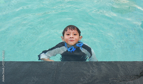 Asian little boy having fun swimming in pool water.