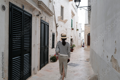 Fototapeta Naklejka Na Ścianę i Meble -  Woman among exterior architecture and decoration at 'LOCOROTONDO' historical white circular labyrinth village of narrow Italian streets- Italy
