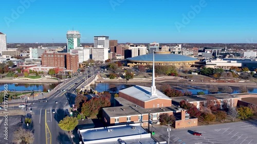 A rotating drone shot, capturing a wide-angle view of the Arkansas River cutting through downtown Wichita, Kansas, with the uniquely shaped Century II Arts Center building, and North Waterwalk bridge. photo