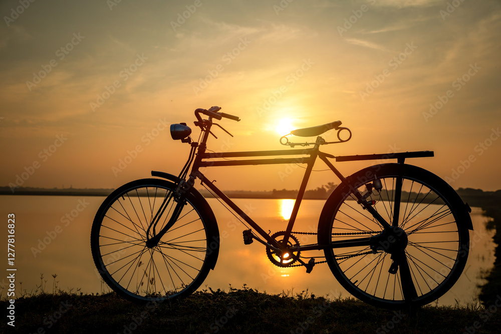 Silhouete of old rusty retro style bicycle stands in a meadow near a lake at sunset. Silhouete of old rusty retro style bicycle stands in a meadow near a lake at sunset.