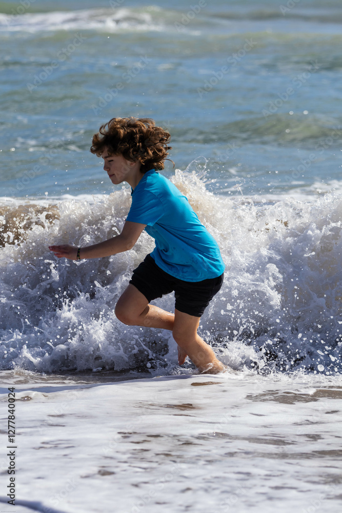 Fototapeta premium Youngster enjoying the ocean. Child runs and plays near the shoreline as waves crash around them on a sunny day at the beach.