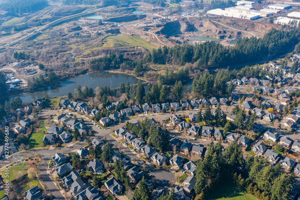 Naklejka premium Aerial drone view of a residential neighborhood in Tualatin, OR, featuring a small lake, tree-lined streets, modern suburban homes, a train track bridge crossing over the water in a peaceful setting