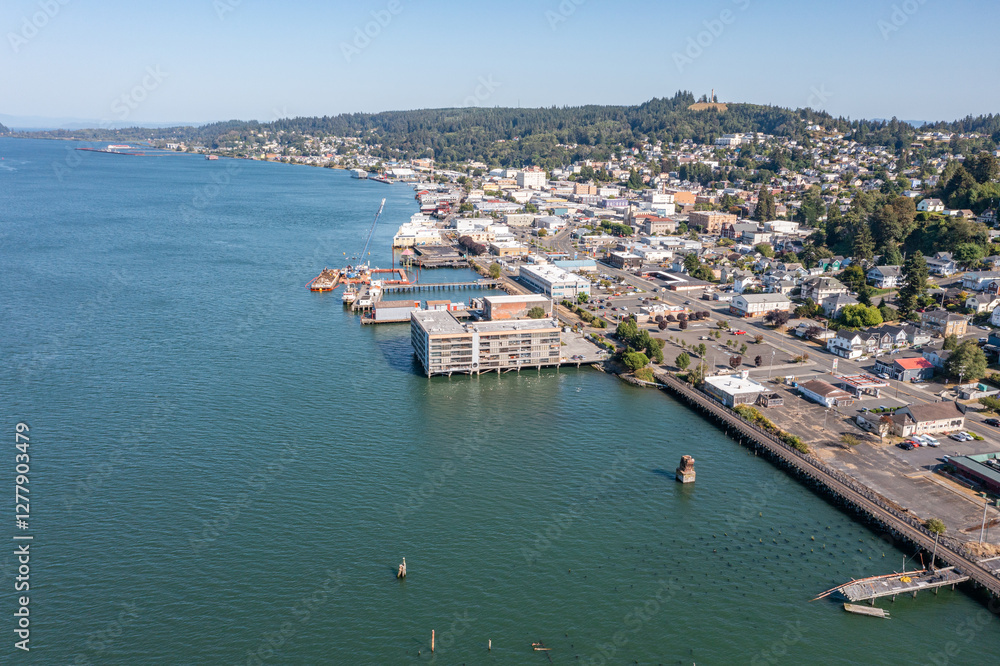 Aerial drone view of downtown Astoria, Oregon, featuring waterfront buildings, the Columbia River, a busy port, fishing boats, and lush hills in the background Aerial drone view of downtown Astoria, Oregon, featuring waterfront buildings, the Columbia River, a busy port, fishing boats, and lush hills in the background