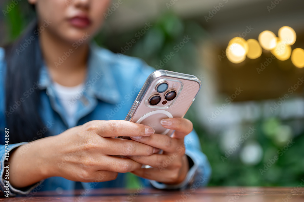 The close up shot of a woman, with face half hiding, holding a pink smartphone on the wooden tabletop. The close up shot of a woman, with face half hiding, holding a pink smartphone on the wooden tabletop.