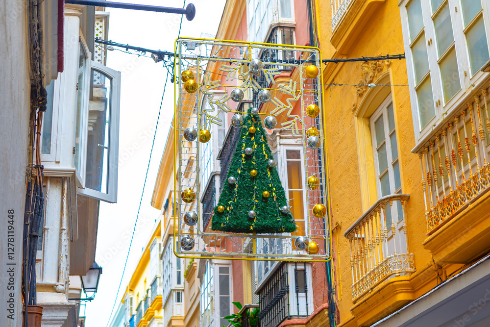 Festive street decoration with Christmas tree and ornaments hanging between historic European buildings. Warm tones of architecture contrast with holiday lights creating charming holiday atmosphere