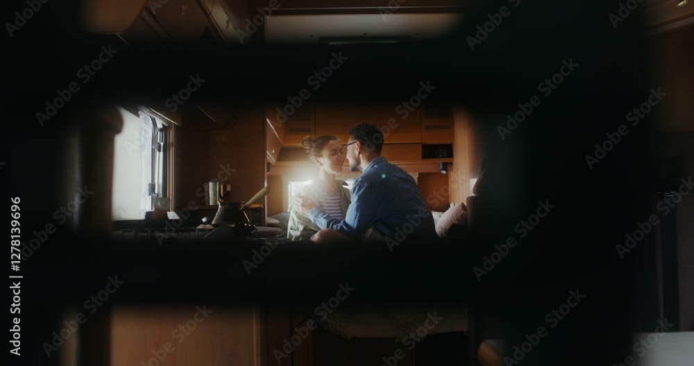 Fototapeta premium A man and a woman smile and kiss sitting on a bed in a van. Romantic trip