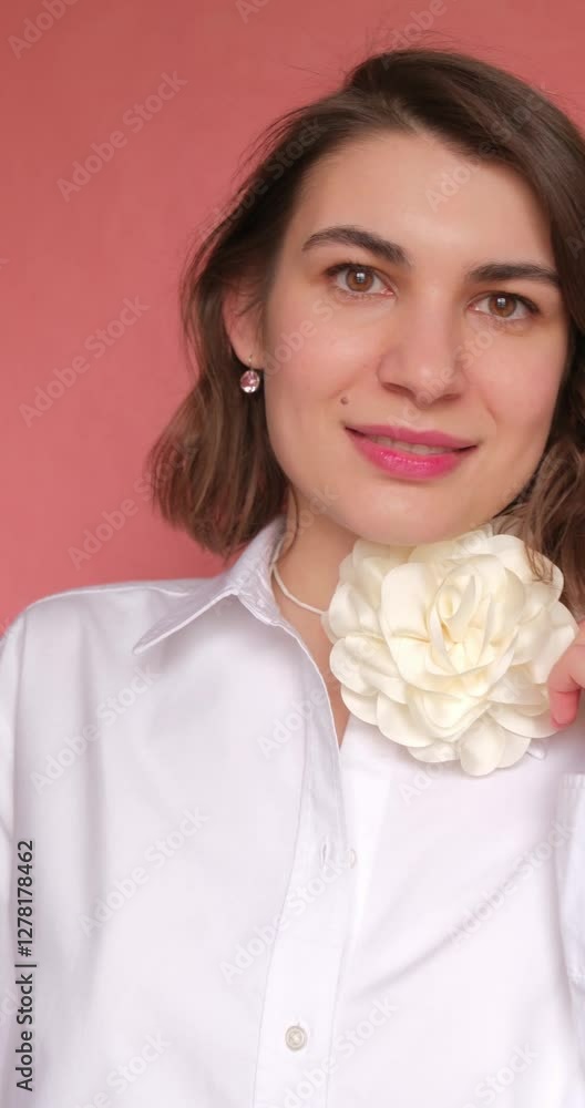Vertical video of beautiful woman in white shirt with rose flower necklace smiling on the pink background