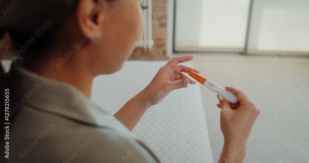 Obraz premium A woman looks at a pregnancy test with two stripes, a view from over her shoulder