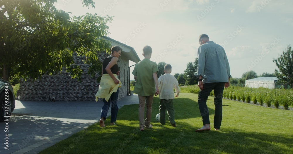 A man, a woman and two children play football in the backyard of their house, family outdoor leisure A man, a woman and two children play football in the backyard of their house, family outdoor leisure