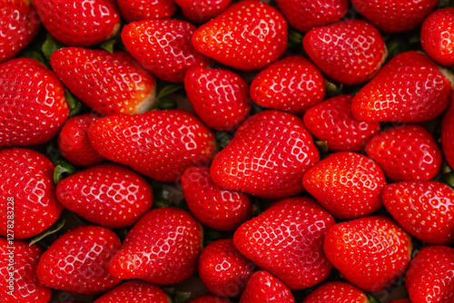Close-up of a group of fresh red strawberries with a shiny texture and visible seeds. The strawberries are piled together, showcasing their vibrant color and juicy appearance