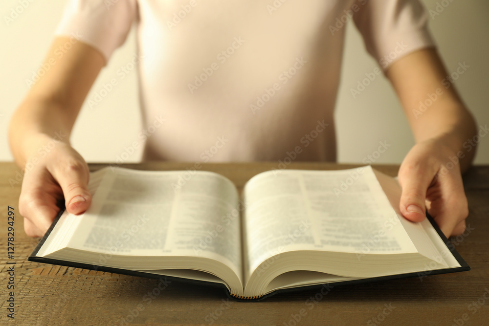 Fototapeta premium Woman reading Holy Bible in English language at wooden table, closeup