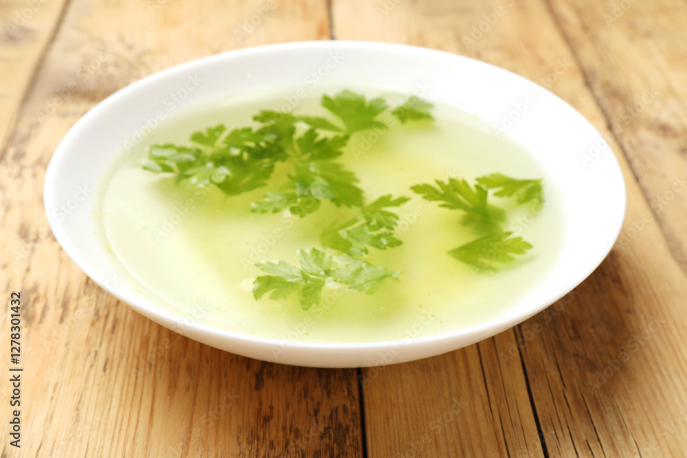 Tasty chicken bouillon with parsley in bowl on wooden table, closeup Tasty chicken bouillon with parsley in bowl on wooden table, closeup