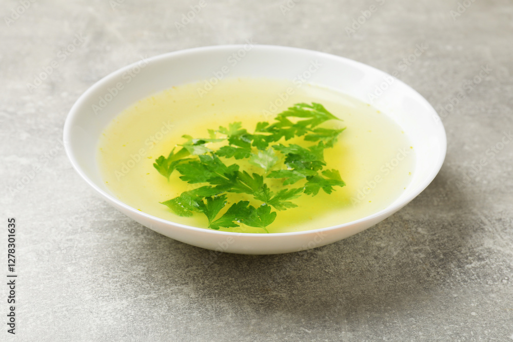 Tasty chicken bouillon with parsley in bowl on grey table, closeup Tasty chicken bouillon with parsley in bowl on grey table, closeup