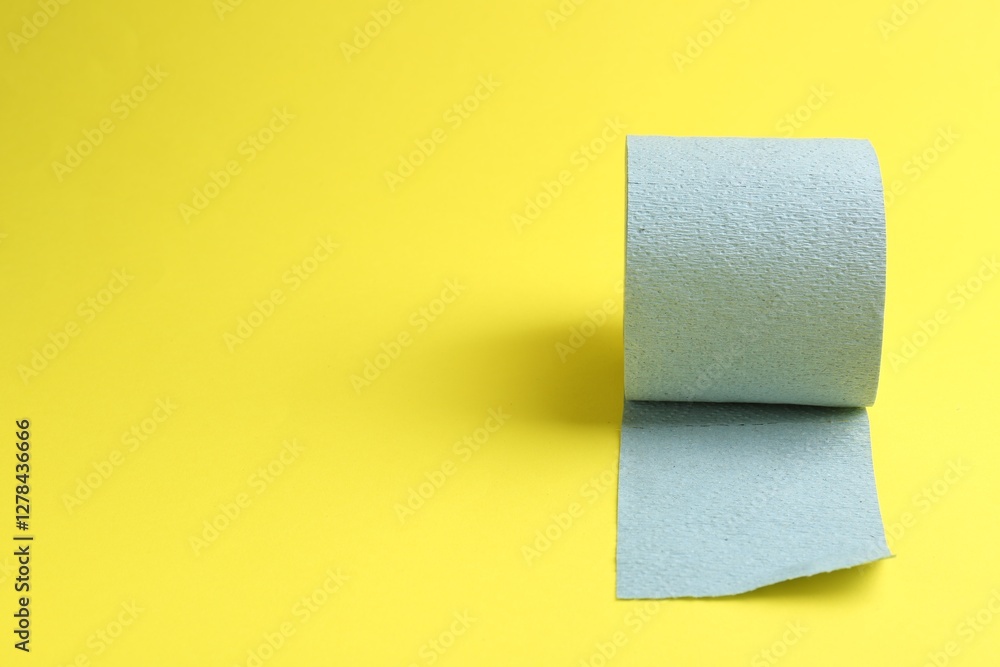 Obraz premium Light blue toilet paper roll on yellow background, space for text