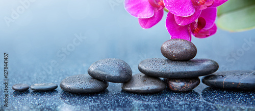 Pink orchid flowers and black spa stones on the gray table background.