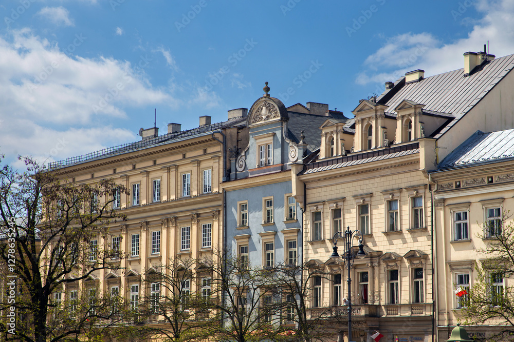 Fototapeta premium A vibrant row of historic townhouses lining the Market Square in Krakow, Poland, under a partly cloudy blue sky.