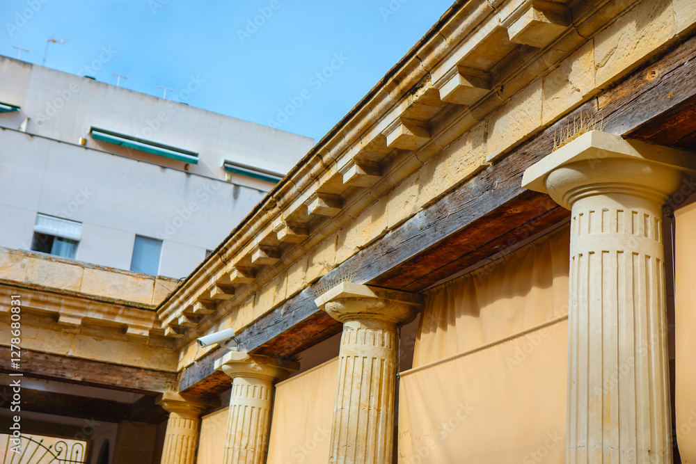 Section of building with classical architectural elements, fluted columns with capitals and a detailed entablature featuring dentil. Ancient Greek and Roman architecture in modern or restored building