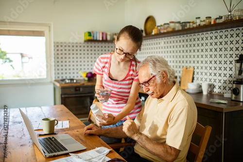 Granddaughter helping grandmother with medication instructions at home kitchen table photo