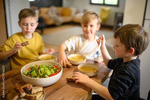 Children enjoy a hearty meal at the table, eating pea soup with croutons and fresh salad. They savor their food with appetite, creating a warm and cozy family dining atmosphere.