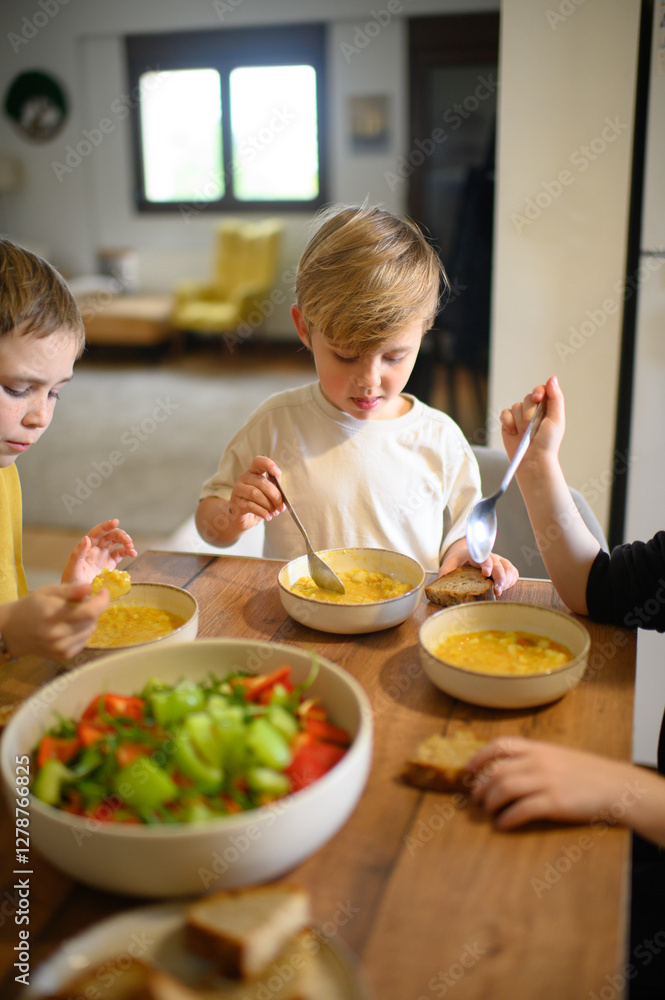 Children enjoy a hearty meal at the table, eating pea soup with croutons and fresh salad. They savor their food with appetite, creating a warm and cozy family dining atmosphere. Children enjoy a hearty meal at the table, eating pea soup with croutons and fresh salad. They savor their food with appetite, creating a warm and cozy family dining atmosphere.