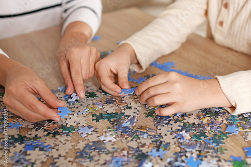 Mother and her daughter solving puzzle together at wooden table indoors, closeup