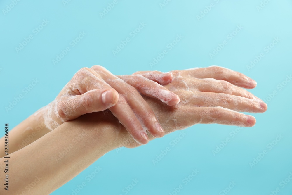 Fototapeta premium Woman washing hands with foaming soap on light blue background, closeup. Hygiene