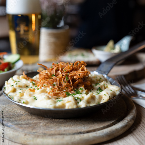 Traditionelle Käsespätzle mit knusprigen Röstzwiebeln, serviert in Gusseisenpfanne im Wirtshaus, bayerische Gemütlichkeit mit frischem Salat und kühlem Bier

