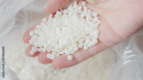 Close-up image of a hand holding small Soy wax white granules, commonly representing raw materials used in manufacturing, such as polymers or other industrial applications. Ideal for illustrating prod