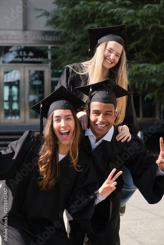 Obraz na płótnie Three cheerful multi ethnic graduates wearing gowns and mortarboards gesturing victory sign celebrating graduation day w salonie