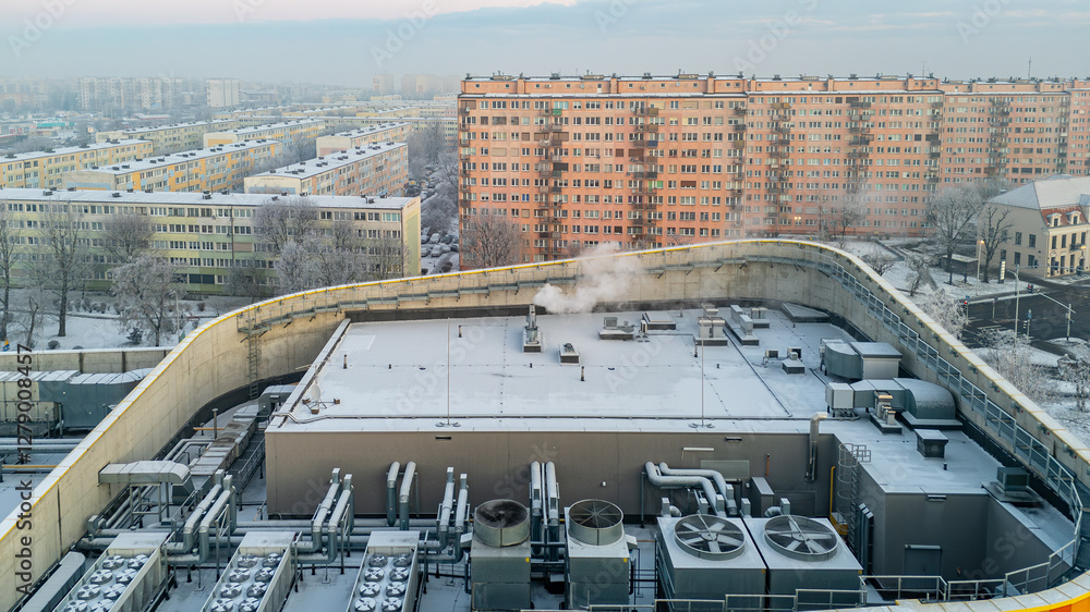 Fototapeta premium winter city landscape from a drone. aerial view of snowy city streets, snowy roofs of buildings on a frosty morning. delicate quiet frosty sunrise over the city. fans and ventilation on the roof