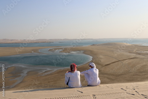 Fototapeta Naklejka Na Ścianę i Meble -  Two Arab people watching the Insland Sea from the height of a dune