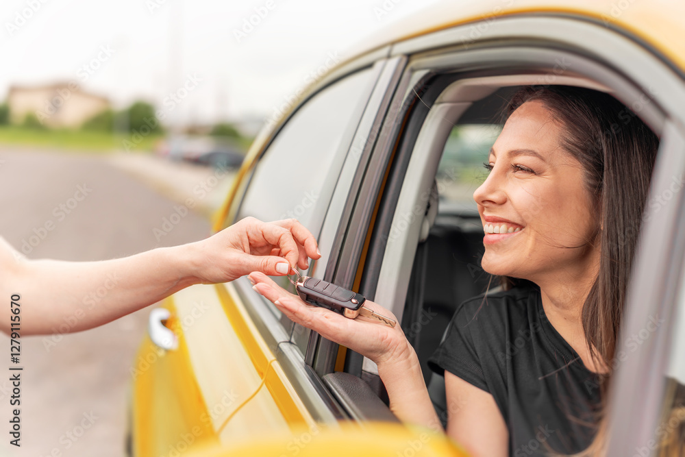 A smiling woman sitting in a yellow car receives a set of keys from another person, symbolizing a car purchase, rental, or ownership transfer.