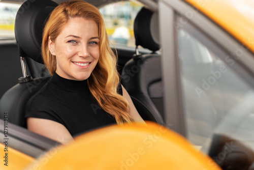 Obraz na płótnie A smiling blonde woman sits in the driver's seat of a yellow car, looking at the camera with a warm and confident expression. w salonie