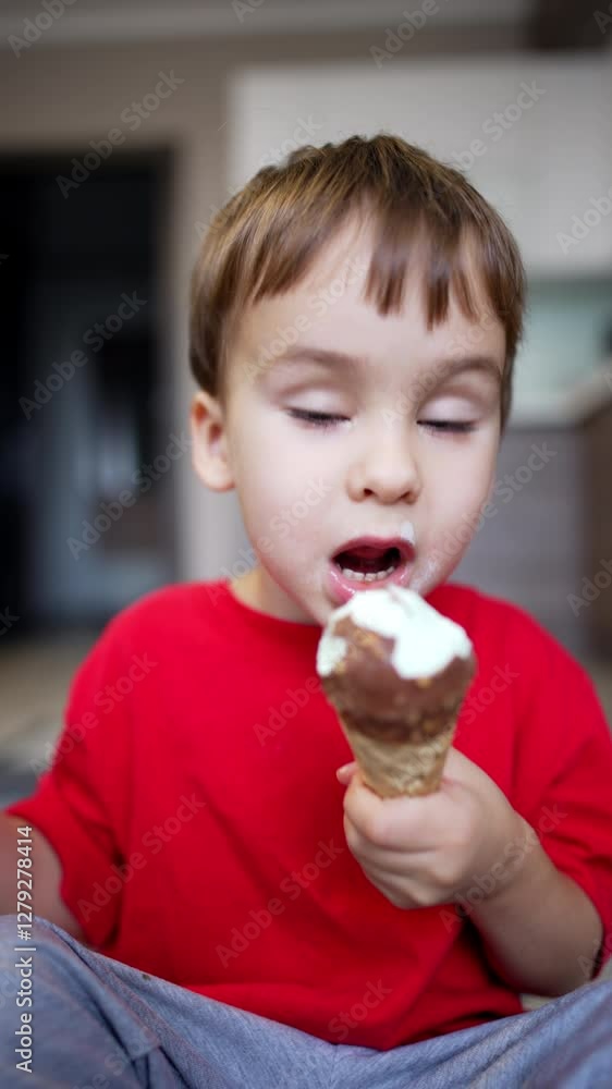 Cute Caucasian toddler boy in red t-shirt eats ice-cream cone. Lovely kid eating dessert. Vertical video. Cute Caucasian toddler boy in red t-shirt eats ice-cream cone. Lovely kid eating dessert. Vertical video.