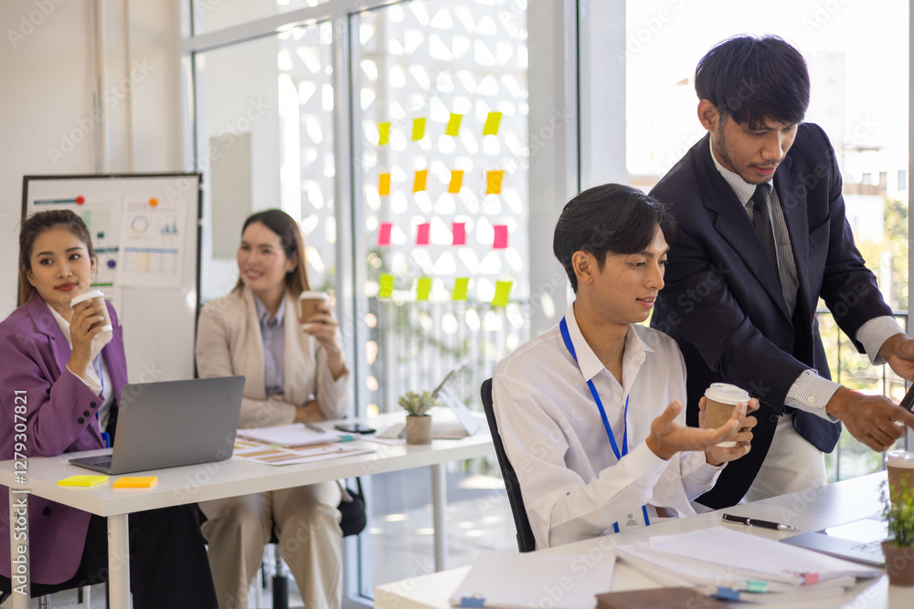 A group of people are sitting around a table with a laptop, a calculator, and a stack of papers. They are discussing business matters and looking at graphs and charts
