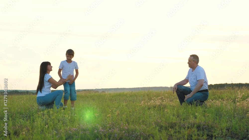 Cute little son runs between mother and father to embrace parents in country field. Happy mother and father spend time with little boy running in rural park. Family with little boy on vacation Cute little son runs between mother and father to embrace parents in country field. Happy mother and father spend time with little boy running in rural park. Family with little boy on vacation