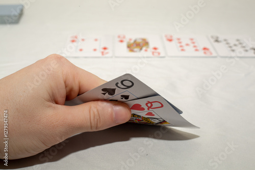 An image showcasing a hand holding playing cards, with more cards laid out in the background. Suggests leisure and gameplay. Suitable for themes like games, recreation, or gambling.