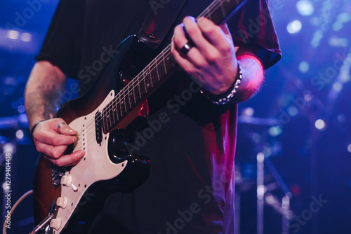 Concert view of an electric guitar player with vocalist and rock band performing in a club, male musician guitarist on stage with audience in a crowded concert show club hall arena, hands on a guitar photo