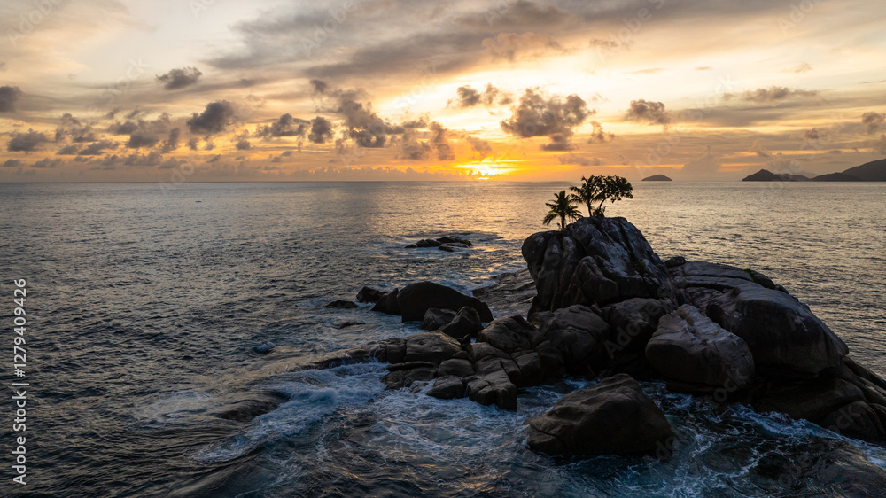 Sunset over the ocean with waves breaking against a rocky shore, creating white foam. Seychelles, Mahe. Sunset over the ocean with waves breaking against a rocky shore, creating white foam. Seychelles, Mahe.