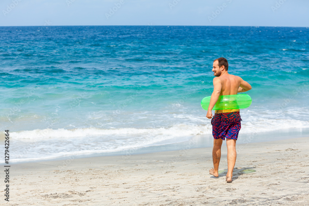Happy bearded hipster in inflatable ring have fun on beach walk. Funny man run along sea surf and jump by water pool. Family travel lifestyle, swimming activities. Summer vacation on tropical island. Happy bearded hipster in inflatable ring have fun on beach walk. Funny man run along sea surf and jump by water pool. Family travel lifestyle, swimming activities. Summer vacation on tropical island.