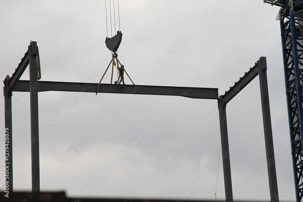 A construction worker on a steel beam in the heights while it is being transported by a construction crane. A man working in the construction. A construction worker on a steel beam in the heights while it is being transported by a construction crane. A man working in the construction.