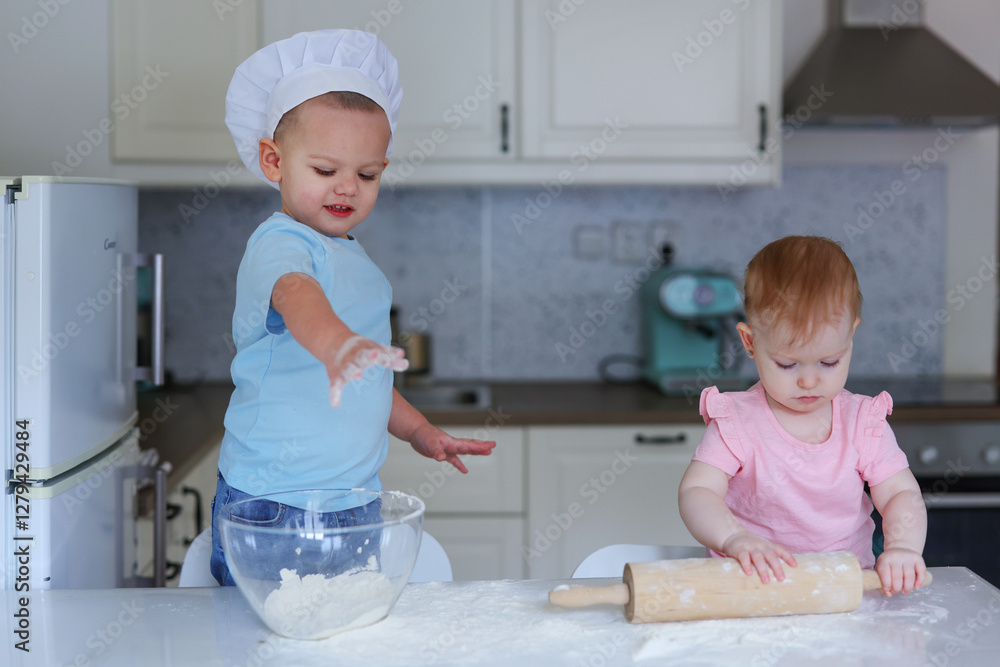 two small children in chef's hats knead flour on the kitchen table two small children in chef's hats knead flour on the kitchen table