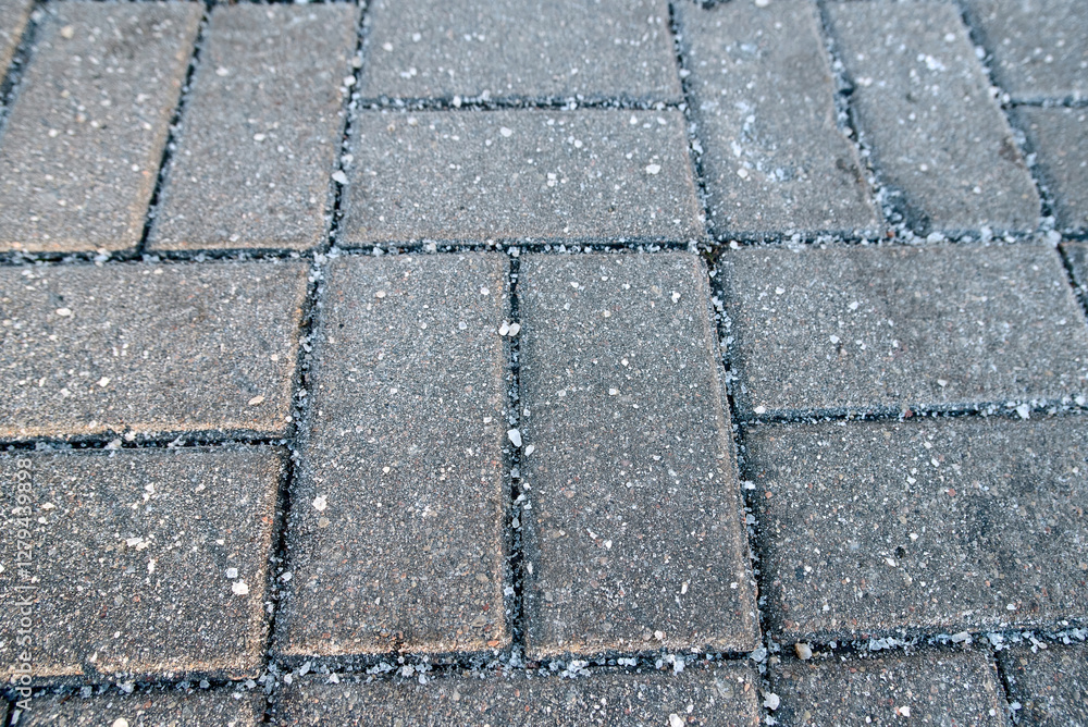 Salt crystals on paving stone slabs in winter, surface treatment methods for preventing ice buildup and slippery hazards. Paving slabs with visible salt crystals in winter season