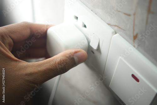 Hand plugging in a charger into a power outlet at home