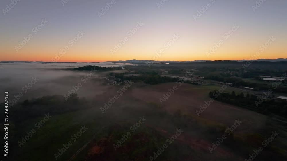 Aerial View of Misty Sunrise Over Johnson City, Tennessee Drone captures stunning sunrise over Johnson City, Tennessee, with mist rolling over countryside and mountains silhouetted against glowing sky Aerial View of Misty Sunrise Over Johnson City, Tennessee Drone captures stunning sunrise over Johnson City, Tennessee, with mist rolling over countryside and mountains silhouetted against glowing sky