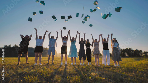 High school students joyfully tossing books in the air to celebrate the end of the school year in a field at sunset