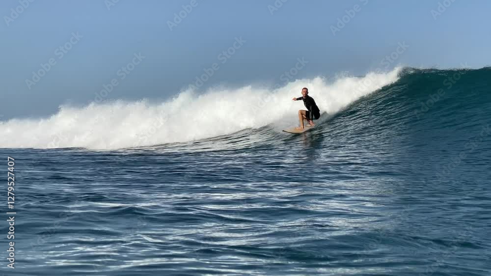 Slow motion video of male adult surfer riding a blue wave in a sea at sunny day.Bali island.Indonesia Slow motion video of male adult surfer riding a blue wave in a sea at sunny day.Bali island.Indonesia