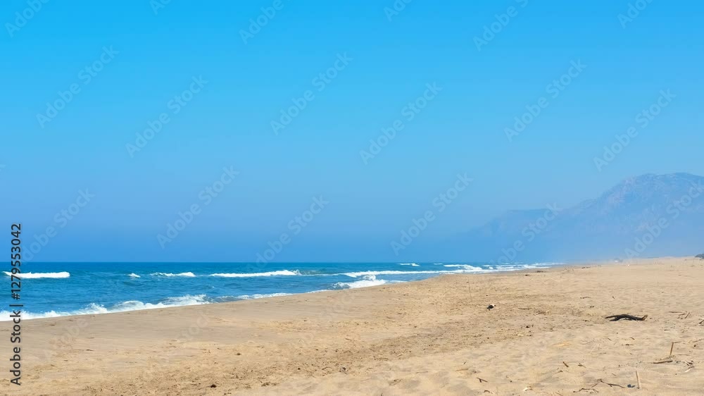 Waves crashing on a deserted beach with mountains in the distance. Turquoise waves crash onto a deserted sandy beach, framed by distant mountains under a bright blue sky. Waves crashing on a deserted beach with mountains in the distance. Turquoise waves crash onto a deserted sandy beach, framed by distant mountains under a bright blue sky.